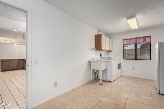 clothes washing area featuring washing machine and clothes dryer, light tile patterned floors, cabinets, and a textured ceiling