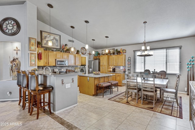 kitchen featuring vaulted ceiling, decorative backsplash, a center island with sink, light tile patterned floors, and appliances with stainless steel finishes