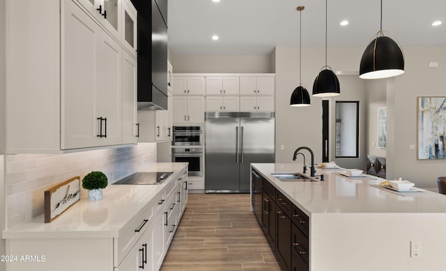 kitchen featuring a sink, hanging light fixtures, appliances with stainless steel finishes, an island with sink, and glass insert cabinets