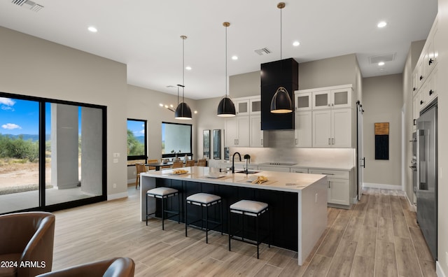 kitchen featuring a center island with sink, white cabinets, glass insert cabinets, decorative light fixtures, and light countertops