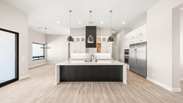 kitchen featuring decorative light fixtures, light countertops, appliances with stainless steel finishes, white cabinets, and a large island with sink