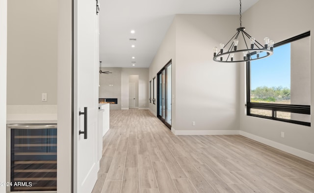 unfurnished dining area with a large fireplace, beverage cooler, baseboards, and light wood-style flooring