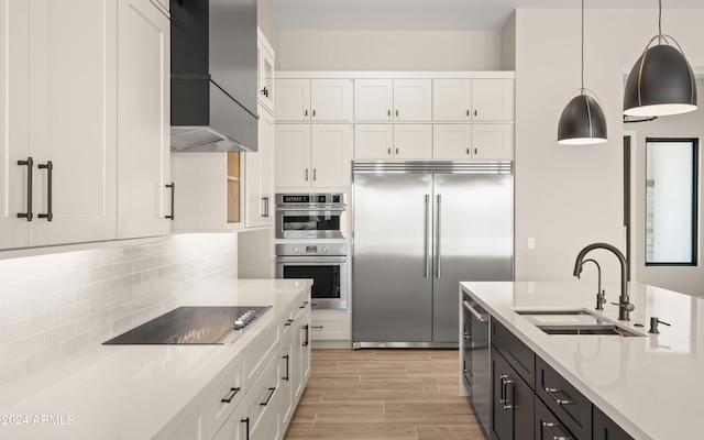 kitchen with white cabinets, wall chimney exhaust hood, hanging light fixtures, stainless steel appliances, and a sink