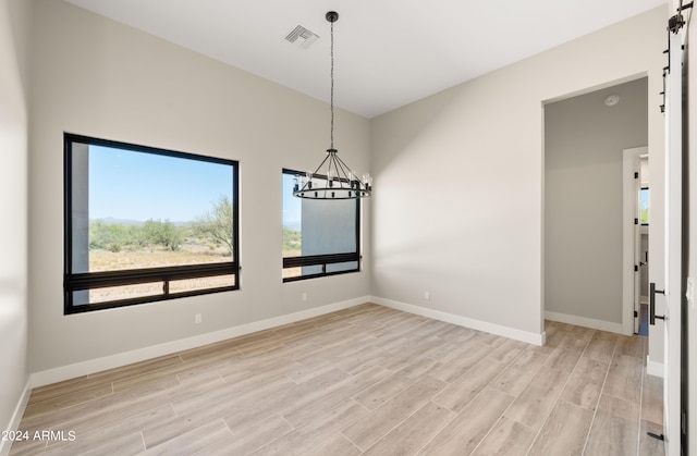 spare room featuring light wood-type flooring, visible vents, baseboards, and an inviting chandelier