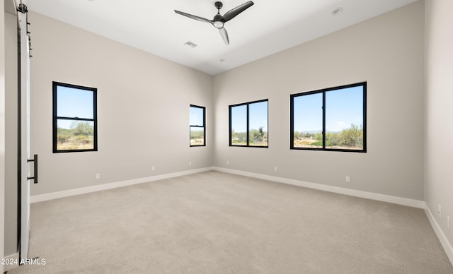 empty room with visible vents, light colored carpet, a ceiling fan, and baseboards