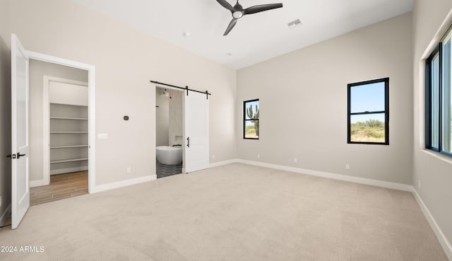 unfurnished bedroom featuring light carpet, a barn door, visible vents, baseboards, and a spacious closet