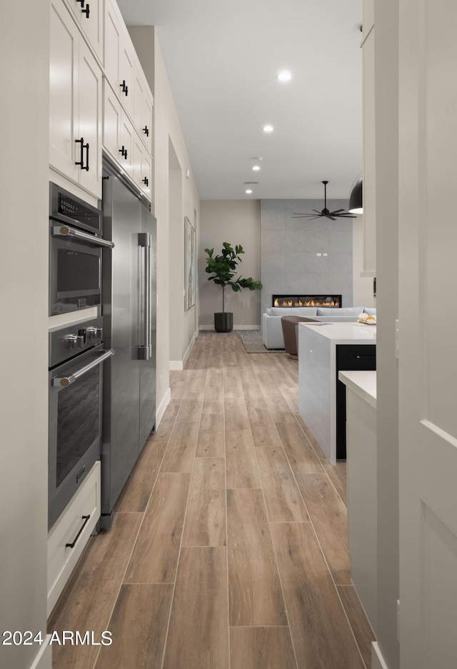 kitchen featuring white cabinets, a tile fireplace, stainless steel appliances, light countertops, and light wood-type flooring