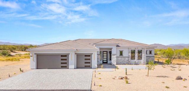 view of front of property featuring stone siding, an attached garage, decorative driveway, a mountain view, and stucco siding