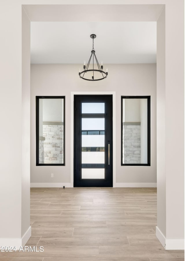 foyer entrance with light wood-style floors, baseboards, and a notable chandelier