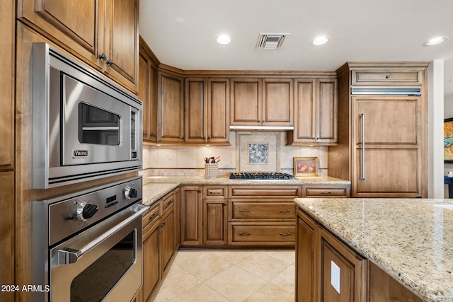 kitchen featuring built in appliances, tasteful backsplash, light tile floors, and light stone counters