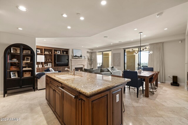 kitchen featuring built in features, a center island with sink, a fireplace, sink, and light tile floors