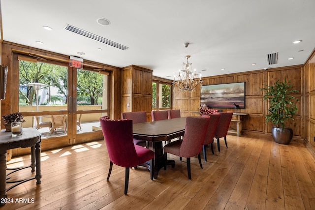 dining room with a healthy amount of sunlight, light wood-type flooring, wooden walls, and an inviting chandelier