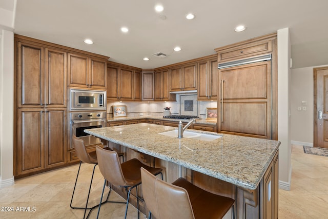 kitchen with built in appliances, a kitchen island with sink, and light stone countertops