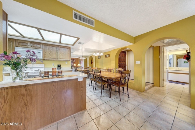 kitchen featuring visible vents, white appliances, arched walkways, light countertops, and light tile patterned floors