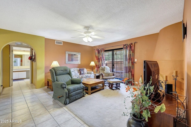 living area with visible vents, a textured ceiling, arched walkways, light tile patterned floors, and ceiling fan