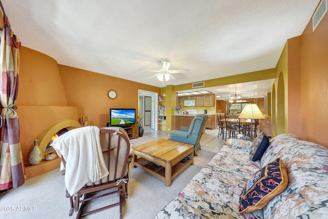 living room with light carpet, ceiling fan with notable chandelier, visible vents, and a textured ceiling