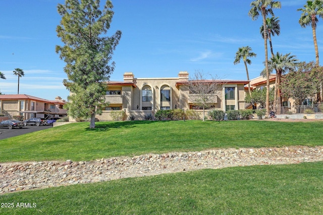 mediterranean / spanish house featuring a front lawn, a chimney, and stucco siding