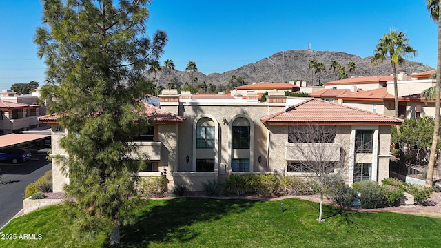 mediterranean / spanish house featuring a tiled roof, stucco siding, a mountain view, and a front lawn