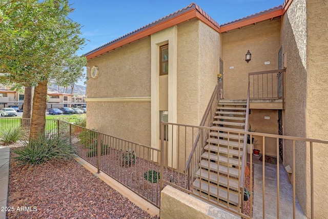 view of home's exterior with a tiled roof, stucco siding, stairs, and fence