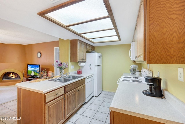 kitchen featuring white appliances, a peninsula, a fireplace, a sink, and light countertops