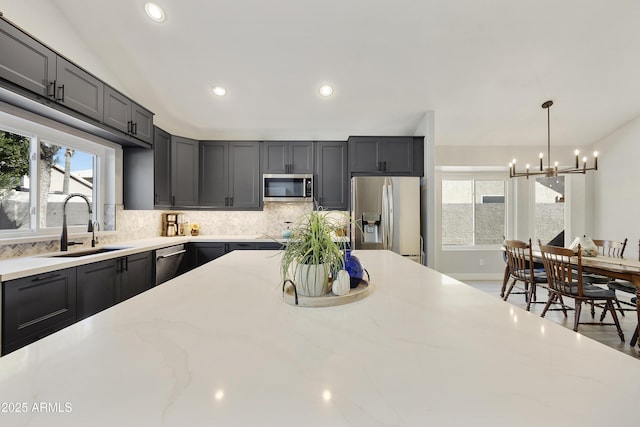 kitchen with decorative backsplash, appliances with stainless steel finishes, light stone countertops, pendant lighting, and a sink