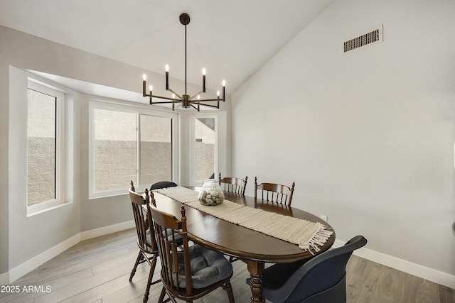 dining area with lofted ceiling, a notable chandelier, visible vents, baseboards, and light wood finished floors