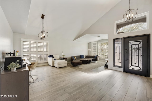 foyer entrance featuring high vaulted ceiling, light wood-style flooring, and a notable chandelier