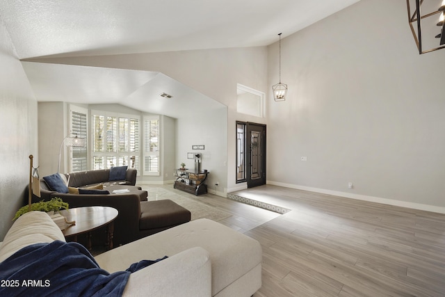 living room with a notable chandelier, visible vents, light wood-style floors, high vaulted ceiling, and baseboards