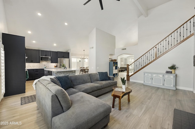 living area with baseboards, light wood-style flooring, stairway, beamed ceiling, and a high ceiling