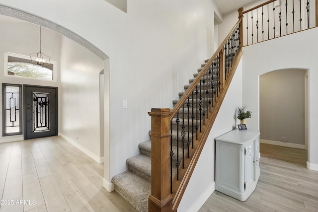 entryway with baseboards, arched walkways, an inviting chandelier, a high ceiling, and light wood-style floors