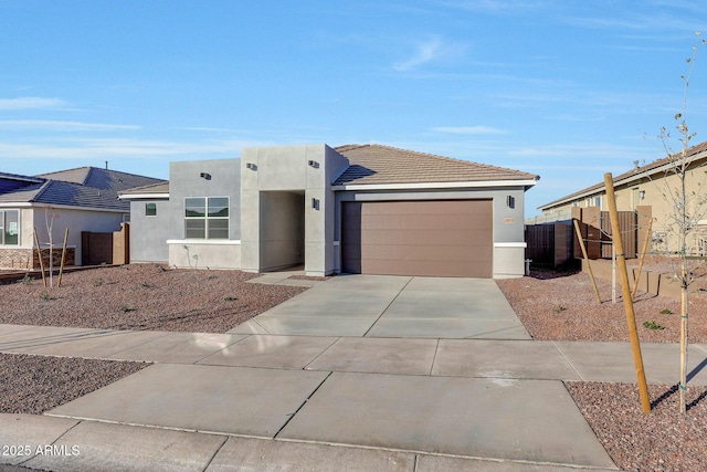 view of front of home featuring stucco siding, an attached garage, concrete driveway, and fence