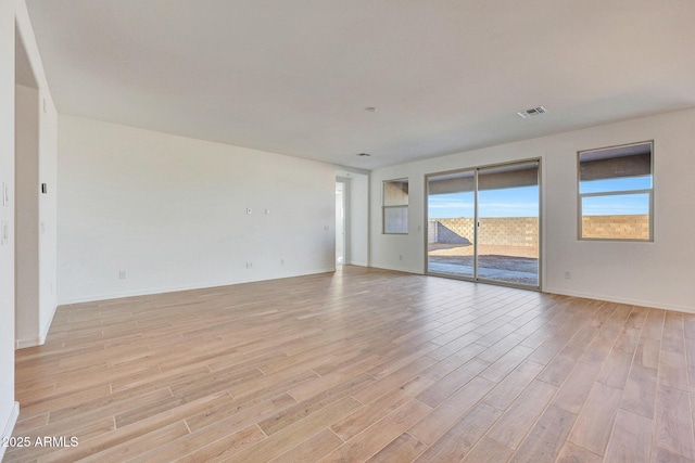 empty room with visible vents, light wood-type flooring, and baseboards