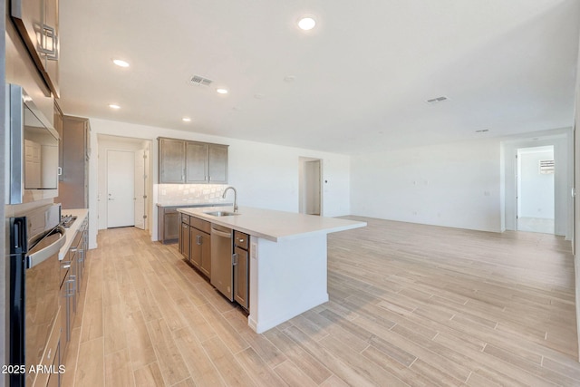 kitchen with stainless steel dishwasher, light wood-type flooring, backsplash, and a sink