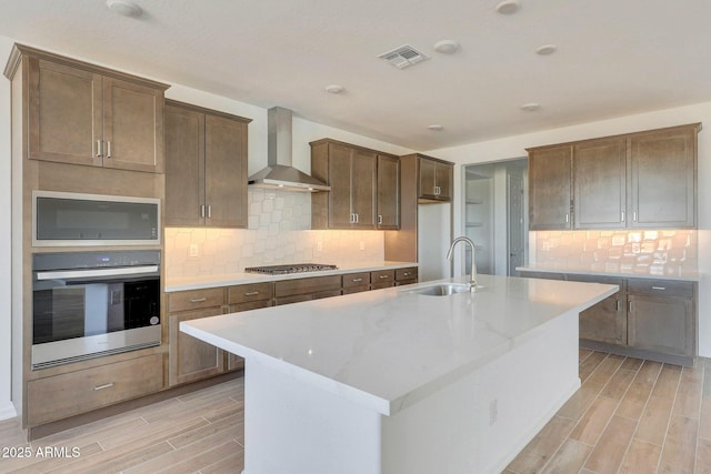 kitchen featuring visible vents, wood tiled floor, appliances with stainless steel finishes, wall chimney exhaust hood, and a sink