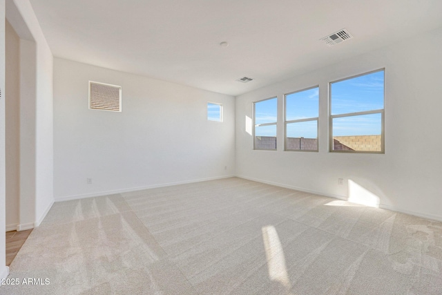 spare room featuring light colored carpet, visible vents, and baseboards