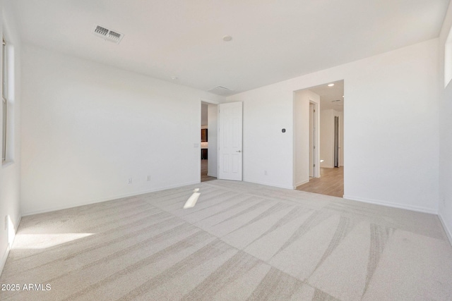 unfurnished room with visible vents, light colored carpet, and baseboards