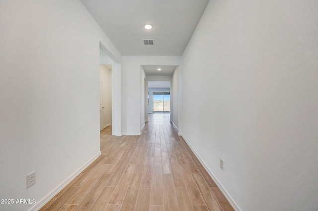 hallway with baseboards, visible vents, and light wood-type flooring