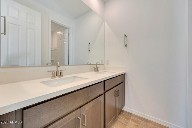 bathroom featuring double vanity, baseboards, wood tiled floor, and a sink