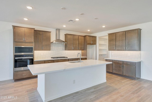 kitchen with visible vents, wood tiled floor, stainless steel appliances, wall chimney exhaust hood, and a sink