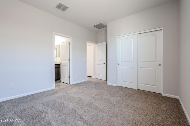 unfurnished bedroom with a closet, ensuite bathroom, and light colored carpet