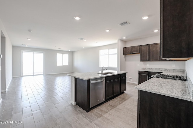 kitchen with stainless steel dishwasher, sink, an island with sink, and light stone counters