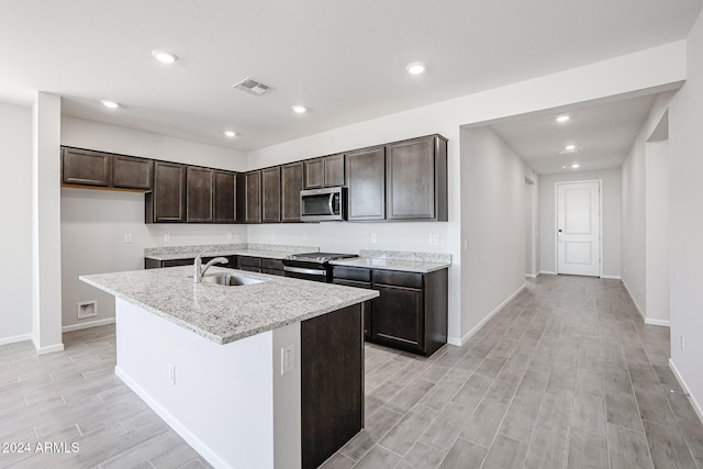 kitchen featuring light stone countertops, sink, appliances with stainless steel finishes, light hardwood / wood-style flooring, and a kitchen island with sink