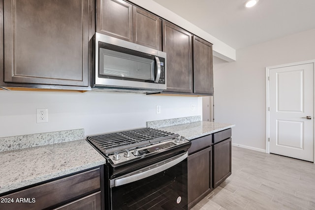 kitchen featuring light stone countertops, appliances with stainless steel finishes, light hardwood / wood-style flooring, and dark brown cabinets