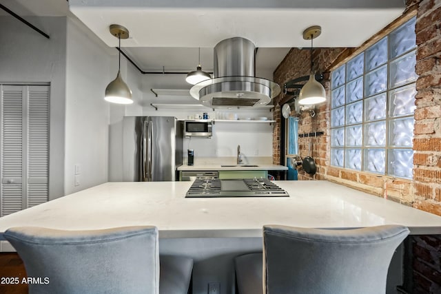 kitchen with brick wall, a sink, light countertops, appliances with stainless steel finishes, and island range hood