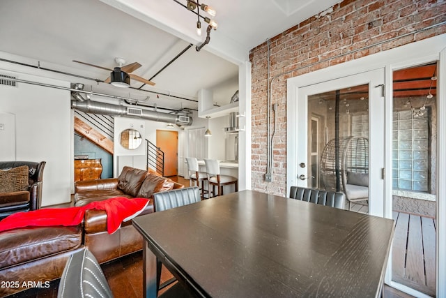 dining room featuring wood finished floors, a ceiling fan, visible vents, and brick wall