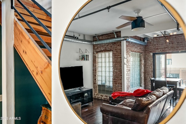 living room with a ceiling fan, track lighting, wood finished floors, and brick wall