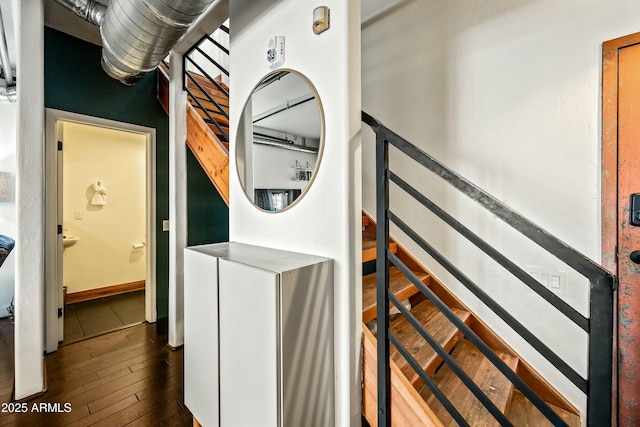 clothes washing area featuring laundry area, stacked washing maching and dryer, baseboards, and dark wood-style flooring