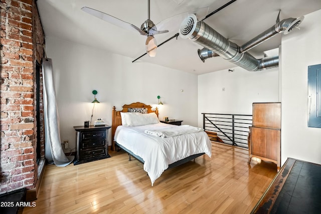 bedroom featuring electric panel, light wood-type flooring, and brick wall