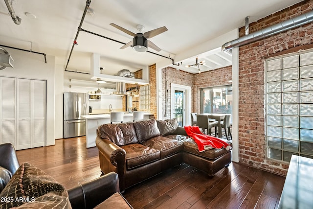 living area featuring hardwood / wood-style flooring, a ceiling fan, and brick wall