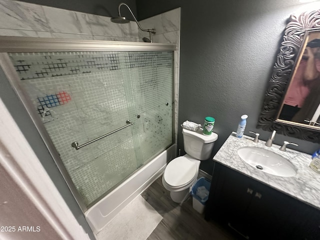 full bathroom featuring hardwood / wood-style flooring, enclosed tub / shower combo, vanity, and toilet